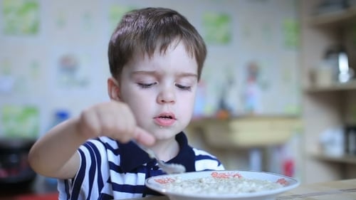 Child Eats Porridge with Spoon in a Kitchen