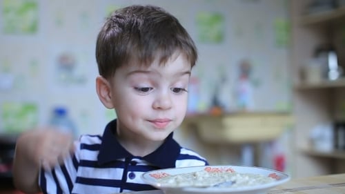Happy Boy Eats Porridge at the Table