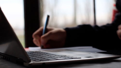 Hands Typing on Laptop and Writing on Paper