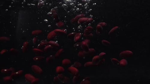 Im Wasser gefallene Bohnen, aufgenommen auf schwarzem Hintergrund. Zeitlupe. Video zum Thema Essen: Bohnen
