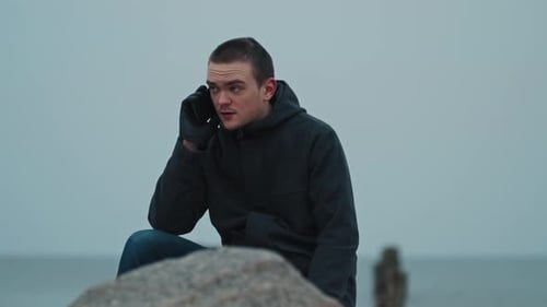 Un joven se sienta en una piedra con el mar azul como telón de fondo
