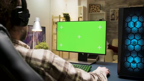 Mann mit Kopfhörern spielt Spiele am Computer mit Greenscreen