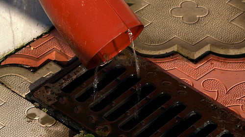 Water Pouring From Red Pipe Into Grate