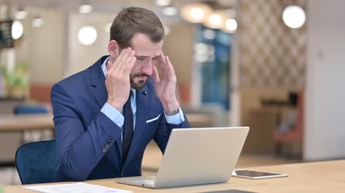 Stressed Businessman with Laptop Having Headache in Office