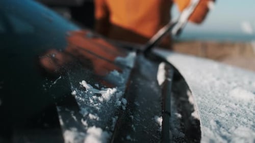 Die Hand des Mannes mit rotem Schaber, um Eis von der Windschutzscheibe des Autos zu entfernen