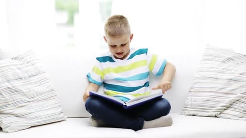 Child Reading a Book on White Couch