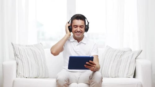 Man with Headphones Smiling Holding Tablet on Couch