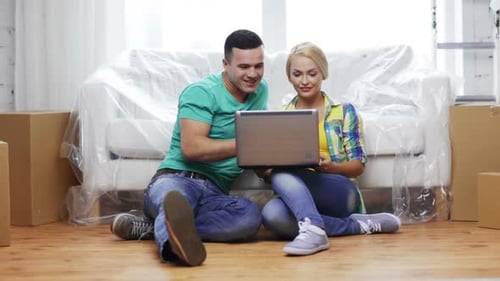 Couple Using Laptop in New Home Surrounded by Boxes