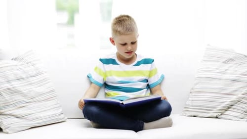 Boy Reading Book on White Couch Indoors