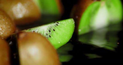 A Piece of Fresh Kiwi Falls Into the Water with Splashes.