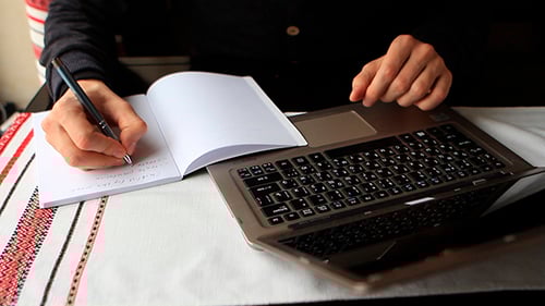 Person Typing on Laptop and Writing in Notebook