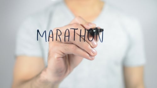 Person Writes Marathon on Clear Glass Surface