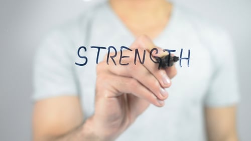 Person Writing Strength on Clear Surface