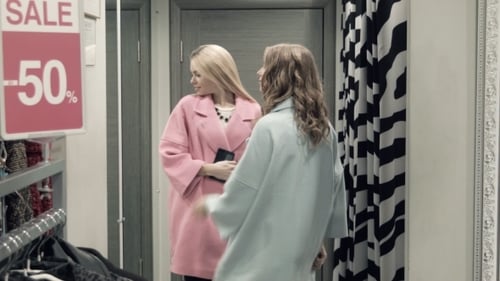 Two Girls Try On a Coat In a Locker Room