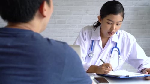 Young Asian Doctor Talking to Patient While Using Laptop and Giving Diagnosis in Doctor's Office