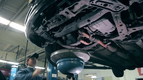 Mechanic Working Underneath Car on Lift in Garage