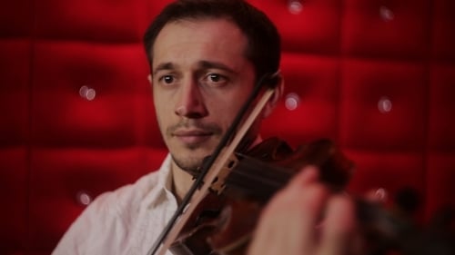 Violinist Performs on Violin in Front of Red Wall