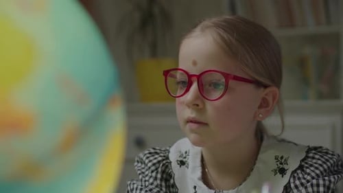 Close Up of Curious Schoolgirl Studying Earth Globe at Home