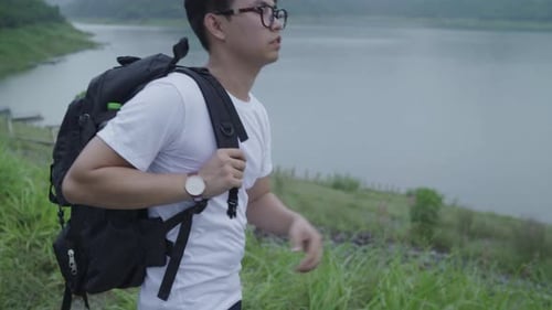 Hiker backpacker man on hiking adventure feeling freedom walking in forest near lake in rainy day.