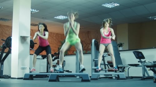 Women Doing Squat Jumps on Step Platforms in Gym