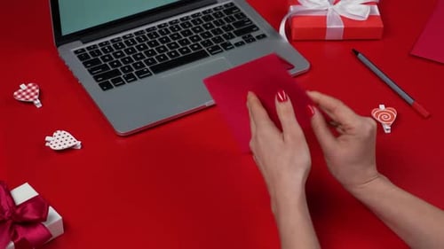 Hands Preparing Love Note on Red Surface
