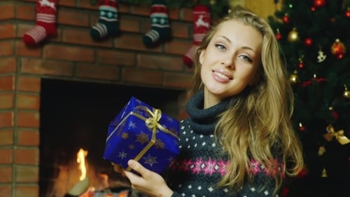 Woman Smiling with Christmas Present by Fireplace