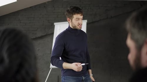 Handsome Young Businessman Pointing at Flipchart During Presentation in Conference Room and Holding