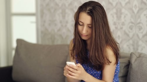 Woman Using Smartphone While Relaxing on Sofa
