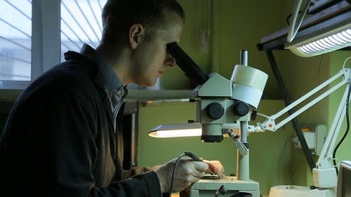 Man Soldering Circuit Board Under Microscope in Workshop