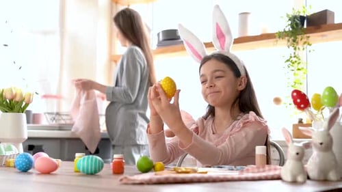 Girl Decorates Easter Egg with Mother in Kitchen