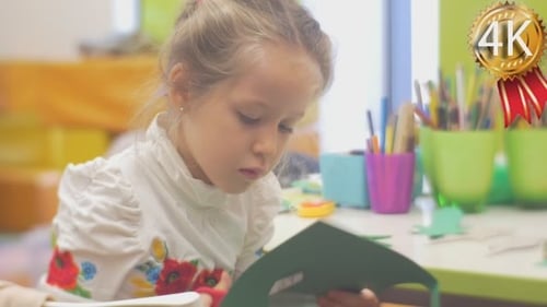 Little Blonde Girl is Sitting and Cutting a Green