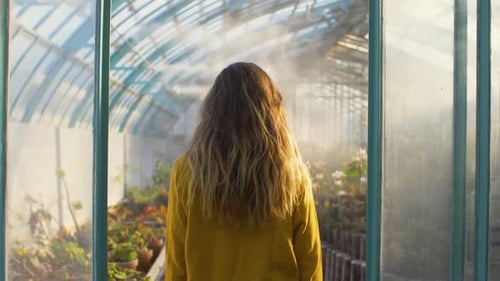 Woman Walking Through a Sunny Greenhouse