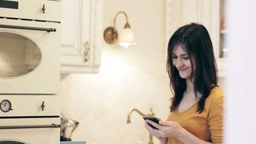 Smiling Woman Using Smartphone in a Kitchen