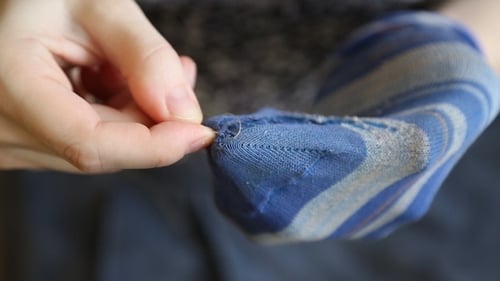 Adult mends torn sock with needle and thread