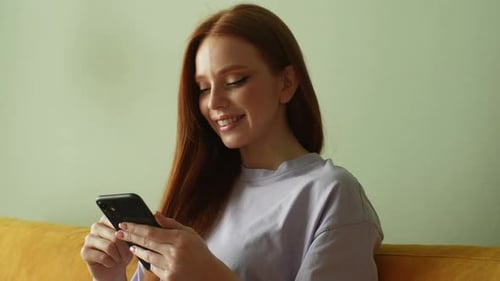 Smiling Woman Uses Smart Phone at Home