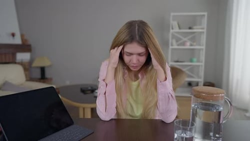 Portrait d'une jeune femme accablée et surchargée se frottant les tempes se tenant tête dans les mains assise à