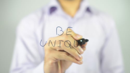 Hand Writes 'Be Unique' on Glass Surface