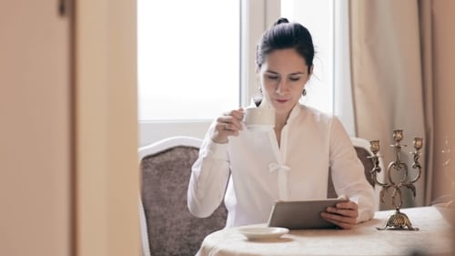 Woman Drinking Coffee and Using Tablet at Table