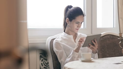 Woman Using Tablet Device While Drinking Tea Indoors