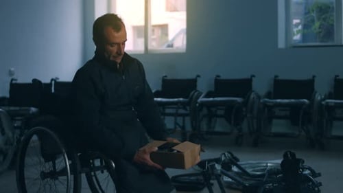 Side View of One American Male Workers in a Workshop at a Factory Making Wheelchairs Sitting at a