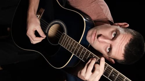 Vertikales Video. Junger Mann spielt eine Akustikgitarre auf schwarzem Hintergrund