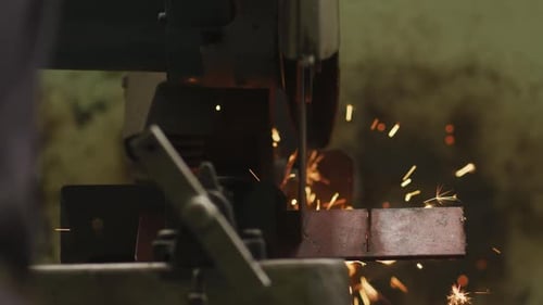 Detail of a Caucasian male factory worker at a factory standing at a workbench and cutting a metal