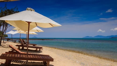 Sonnenschirme und Stühle auf goldenem Sand vor dem azurblauen Meer