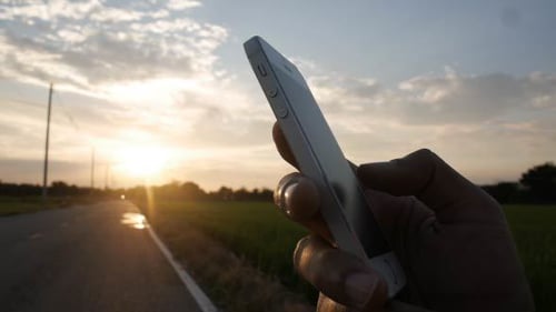 Hand Using Phone at Rural Sunrise