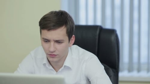 Stressed Young Professional Working at Desk on Laptop