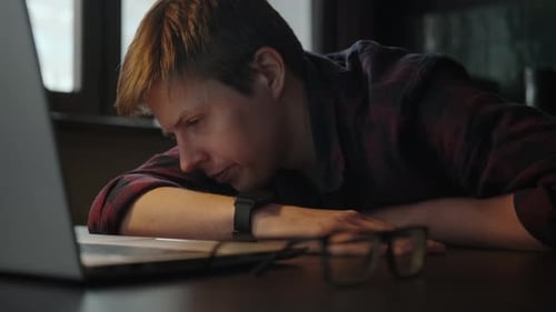 Tired Young Adult Works on Laptop at Desk