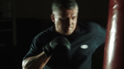 Muscular Man Punches Heavy Bag in Dark Gym
