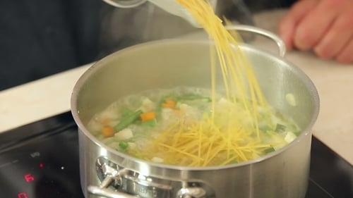 Preparing Steaming Vegetable Soup with Noodles in Kitchen