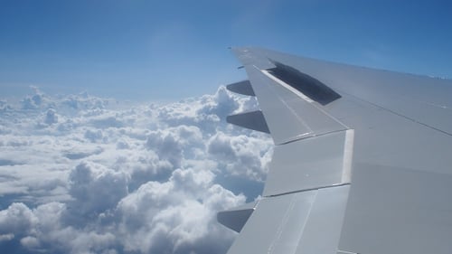 Airplane Wing Above Fluffy Clouds on Sunny Day