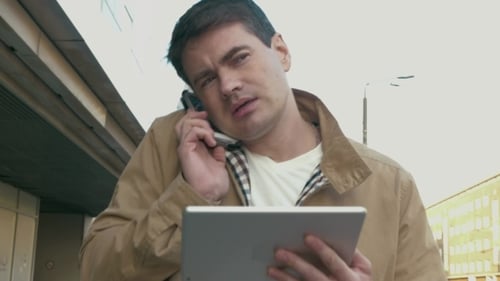 Man Using Tablet and Talking on Phone Outdoors